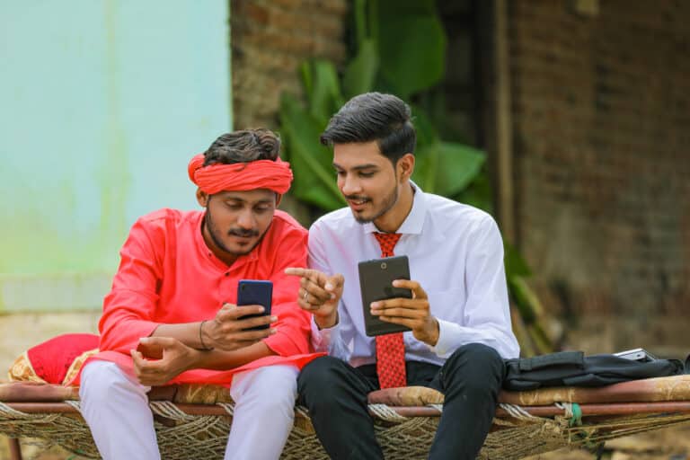 Young indian agronomist or banker showing some information to farmer in smartphone