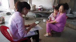 Two women sitting on chairs during an interview - one is carrying a tablet, the other has a child on her lap