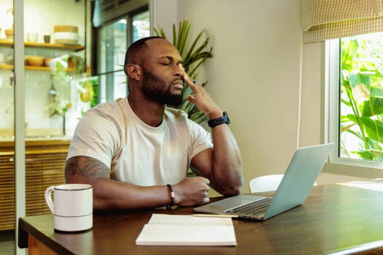 Stressed African adult male works on laptop.