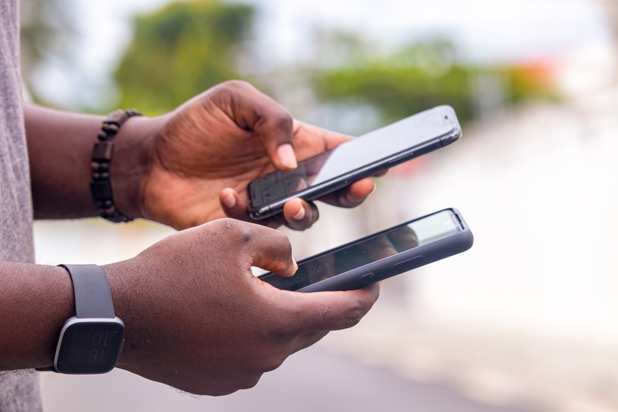 Hand of a young black african man seen from the side holding a smartphone at a construction site in the city