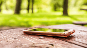 Macro closeup of lost generic light pink rose gold smartphone, phone left, in plastic clear case lying on table outside.