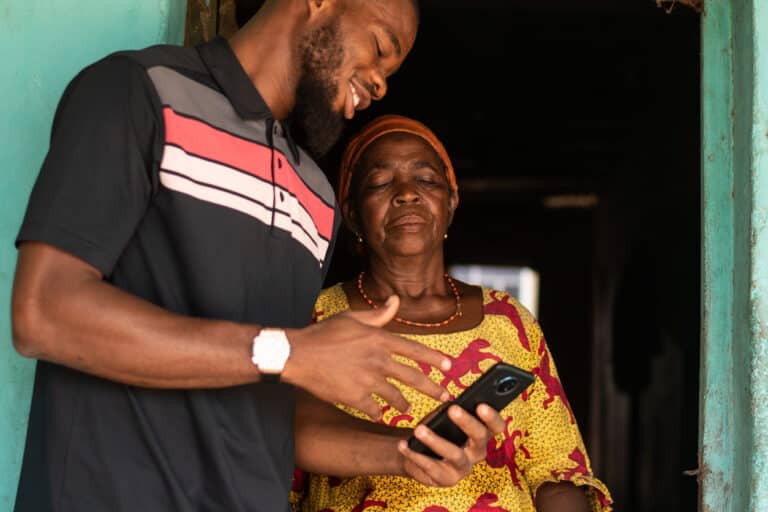 A young African man explaining to an elderly African woman how to use a mobile device.