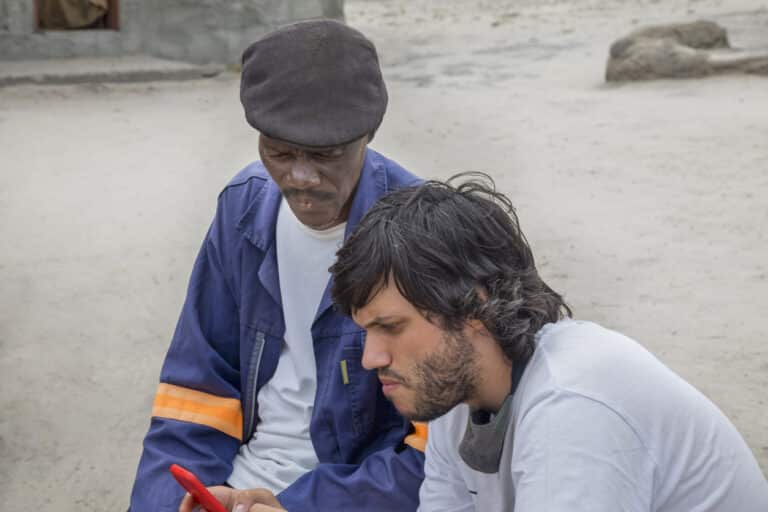 two men talking and discussing the phone screen in an African village