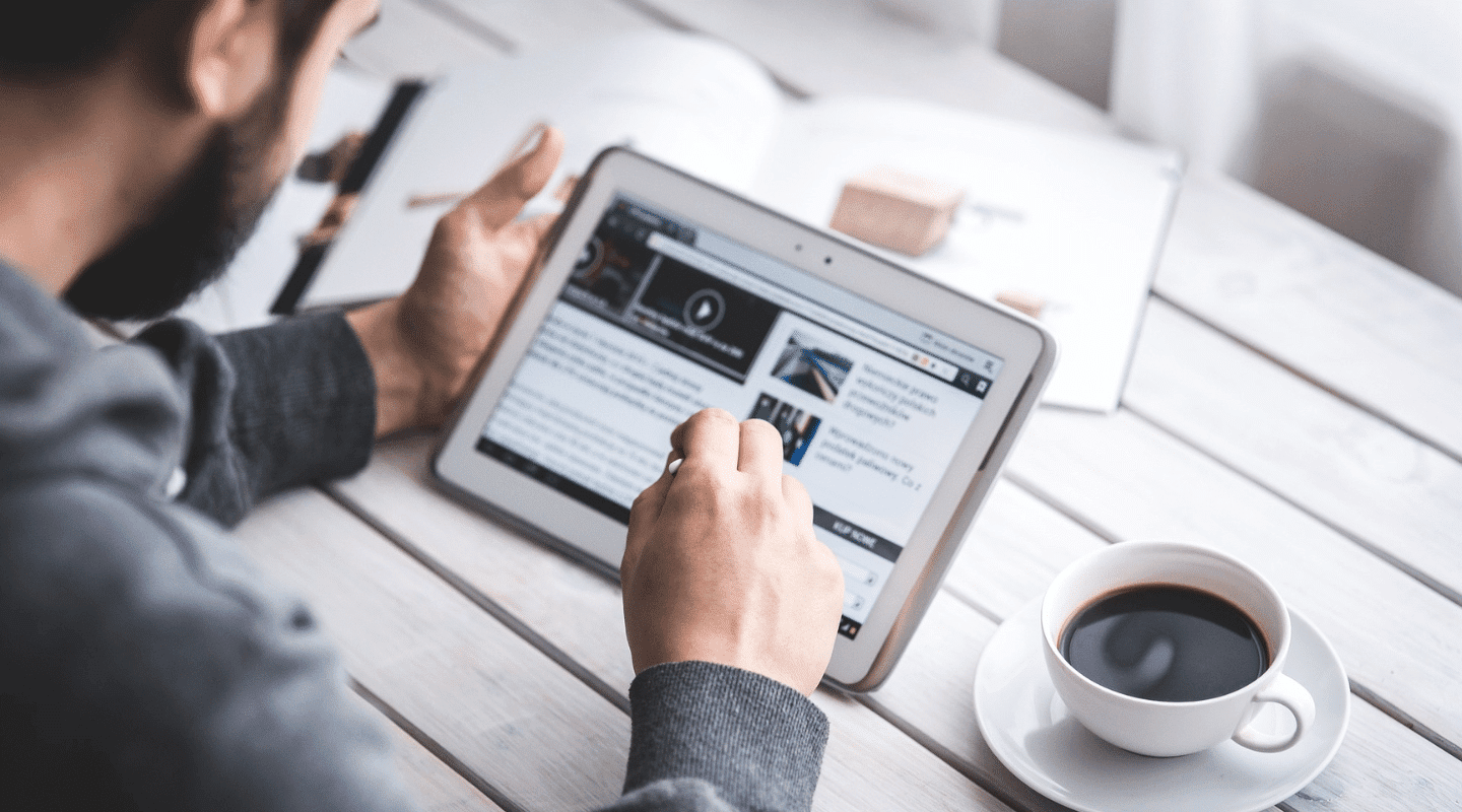 A man uses a tablet while sitting at a table drinking a coffee.