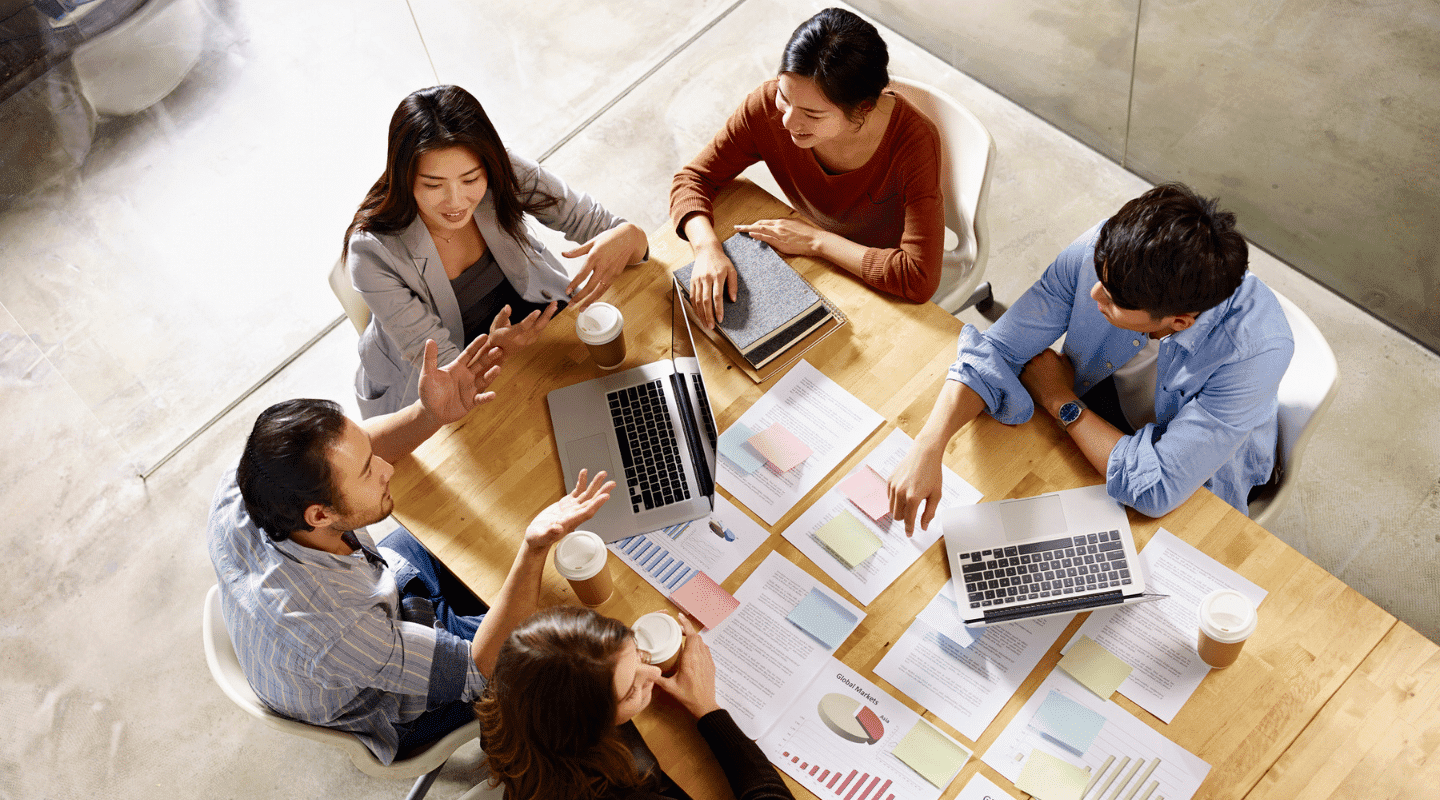 Diverse group of colleagues sit around a table, representing the roles and responsibilities of data governance.